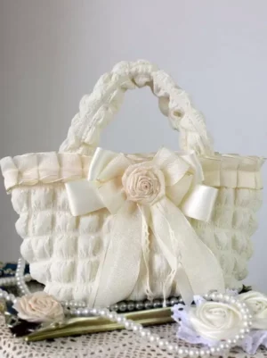 Cream satin bow rococo lolita handbag with fabric rose and ruffled woven handles, displayed on vintage lace mat with pearls and decorative flowers, sweet lolita tote