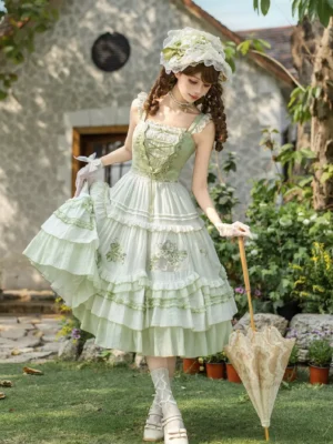 Green sweet lolita dress with tiered ruffles and floral embroidery front three-quarter view outdoor garden setting with matching bonnet headwear vintage parasol and arm accessories