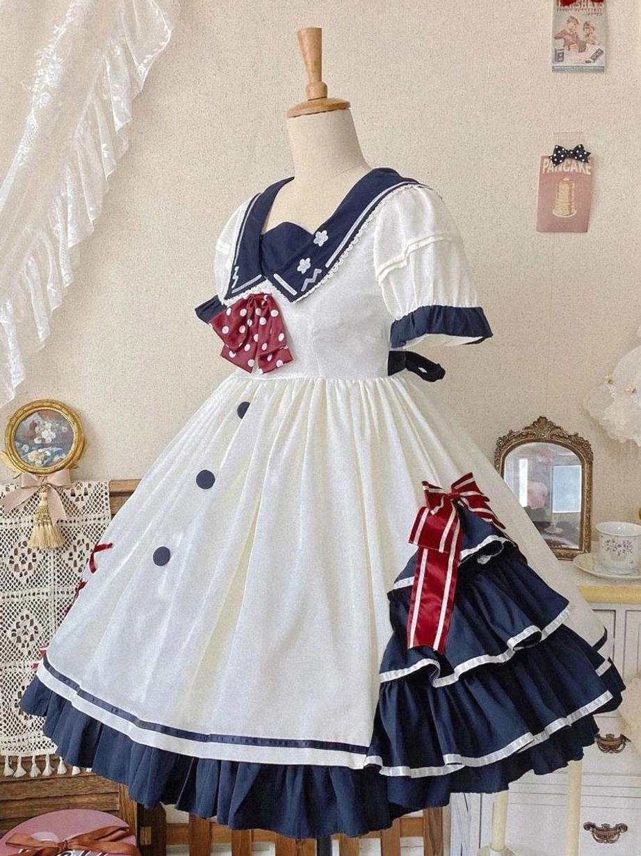 white sailor sweet lolita dress three quarter side view on dress form displaying layered ruffled skirt with red ribbon detail and navy sailor collar trim