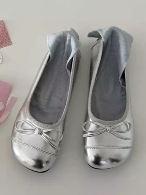 Silver ballet flat Lolita pumps with delicate bow vamp detail, glossy metallic finish, round toe design, top-down flat lay product shot