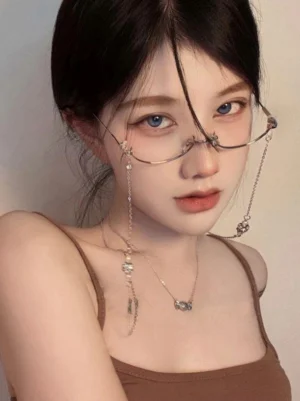 Silver-toned eyeglass chain with spherical decorative charms and crystal accents on model wearing half-rimless frames, frontal portrait