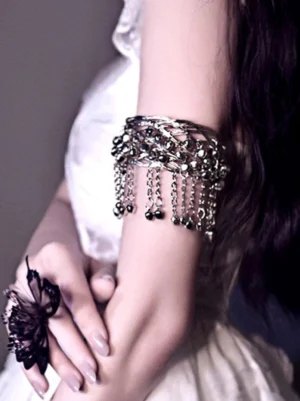 Silver filigree bell tassel arm cuff worn on upper arm with dangling chain tassels, modeled on female in white lolita dress, side close-up view showcasing hollow filigree band and polished bell charms