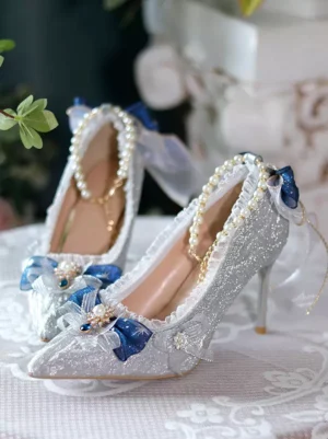 Pointed-toe Lolita bridal pumps side three-quarter view showing stiletto heel and ruffled pearl collar trim detail on lace table with greenery