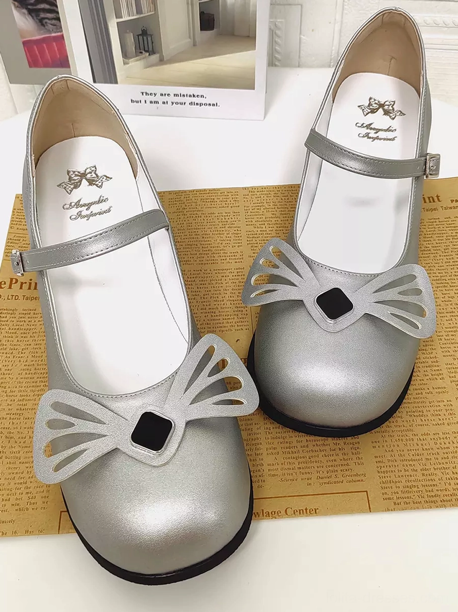 Paired silver Lolita Mary Jane shoes dual front top-down view on vintage newspaper background displaying insole branding, black square bow detail, black outsole, and ankle straps