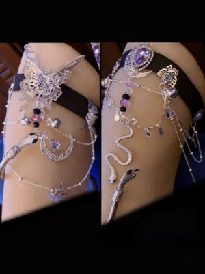 Silver snake butterfly moon gem layered thigh garter with purple gem accents on black elastic band, featuring intricate beaded chain details and carved metal charms - worn on mannequin leg in gothic lolita style