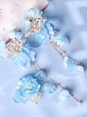 Sky blue gradient flower tassel hair comb with pearl details and golden base, displayed in oblique top-down view on light blue desktop with decorative book