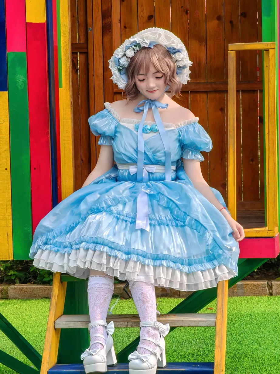 Seated side front view of sky blue lolita dress showcasing floral-decorated bonnet, ruffled skirt trim details, and off-shoulder neckline at amusement park ladder location
