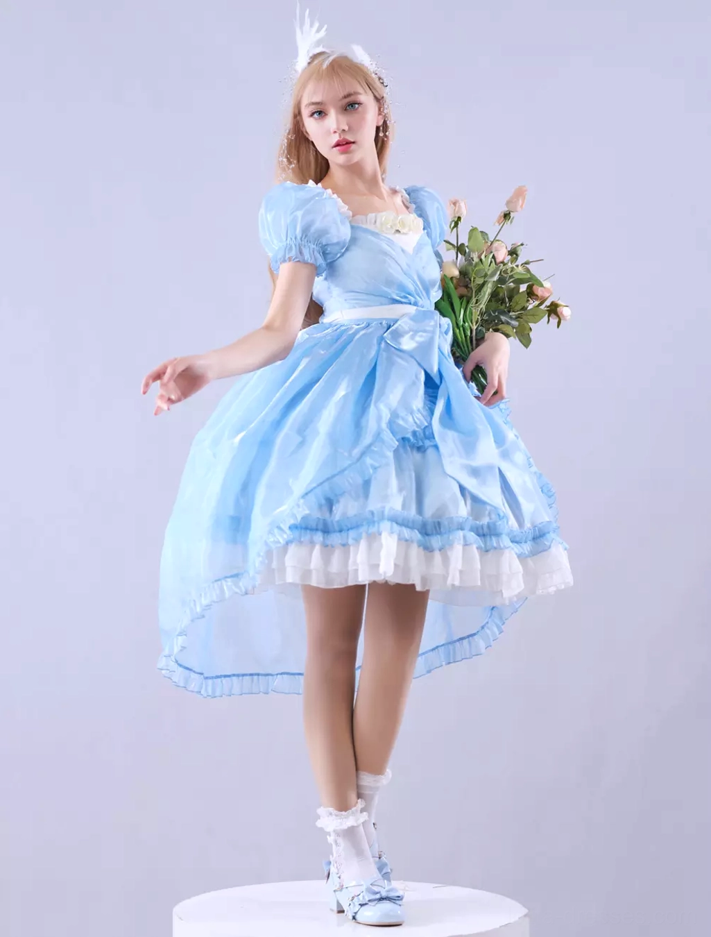 Three-quarter side view of sky blue sweet lolita dress with wearer holding flower bouquet, decorative waist satin bow, high-low hem, and romantic fairy tale aesthetic in studio background