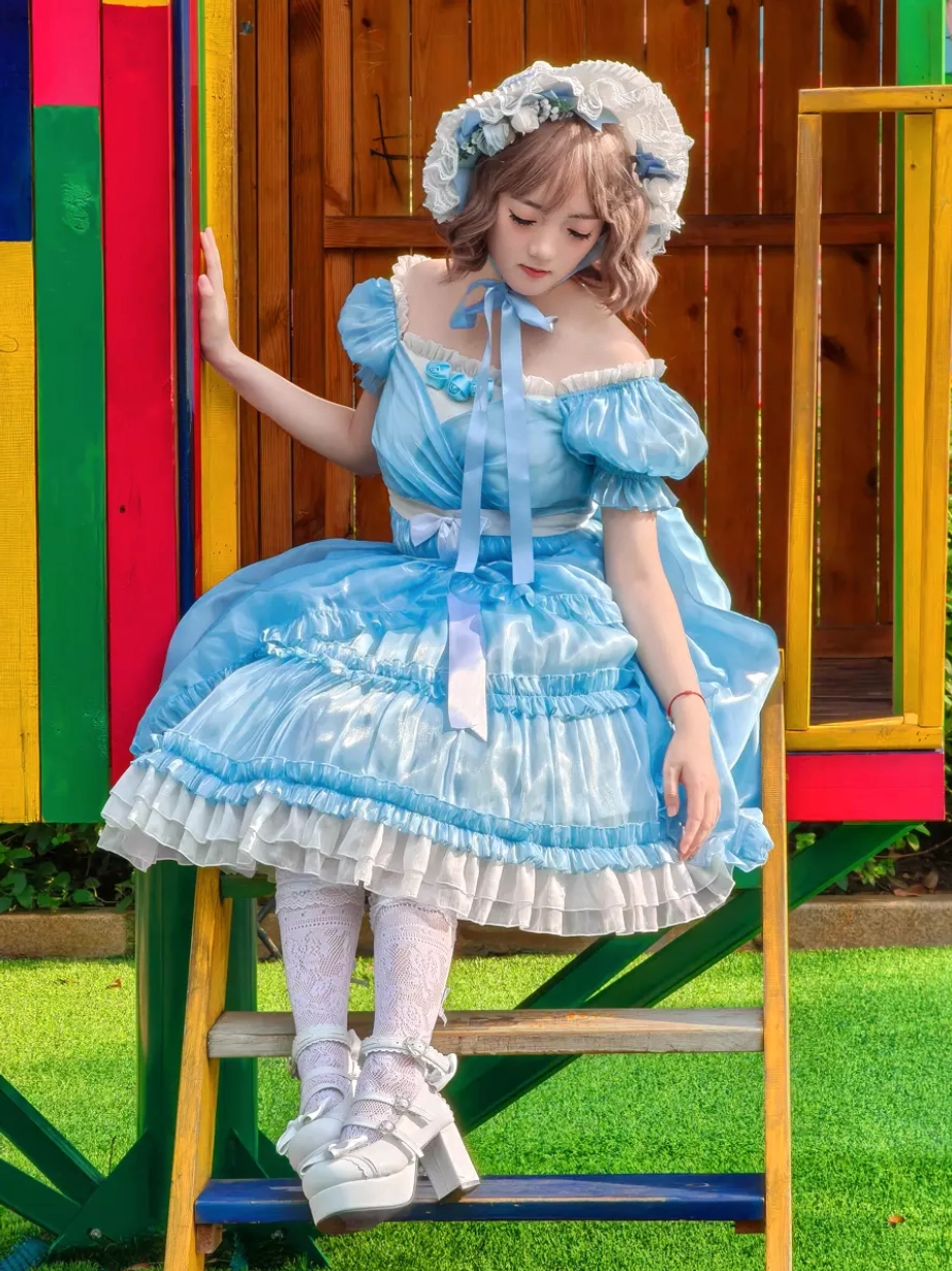 Side seated pose of sky blue sweet lolita dress highlighting off-shoulder neck ribbon, layered ruffled skirt construction, and voluminous puff sleeves at amusement park stairway