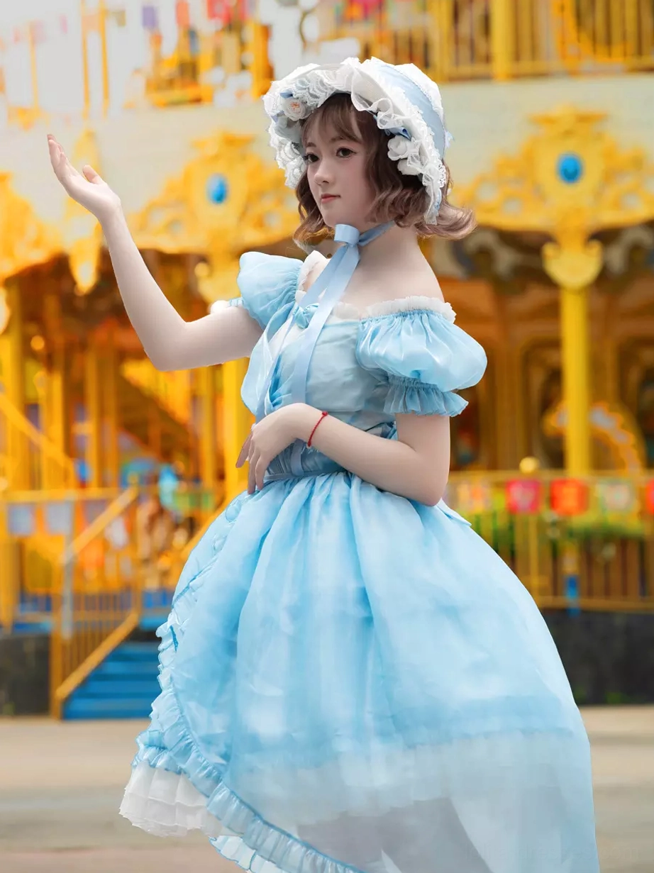 Side front view of sky blue sweet lolita dress featuring satin neck bow, puff short sleeves with ruffled trim, and complete silhouette at amusement park location