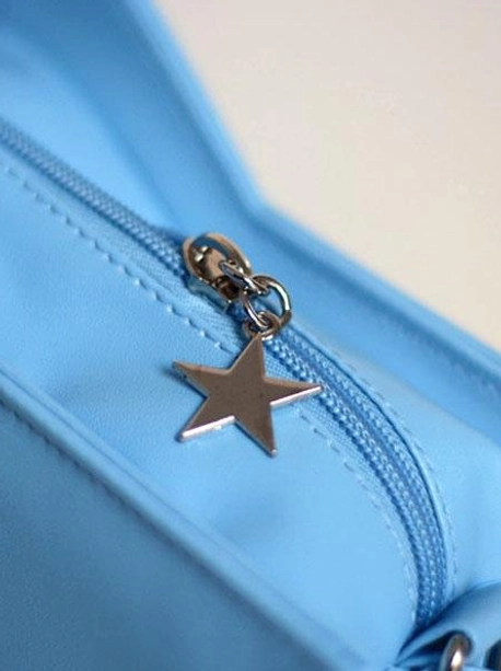 Close-up macro shot of star-shaped metal zipper charm and pull on lolita crossbody bag with matching blue stitching blue zipper tape and smooth faux leather fabric