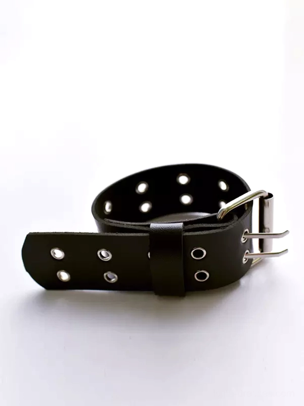 Unassembled flat lay view of black leather arm strap showing dual-prong silver buckle and complete adjustment eyelet system