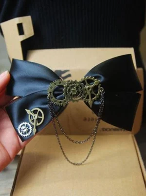 Steampunk lolita hair clip with black satin bow and vintage metal gears held in hand against kraft paper background showing chain details