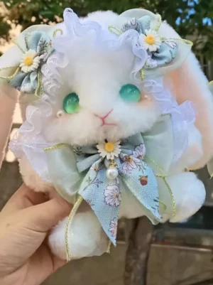 Sweet bunny plush crossbody bag with light blue daisy bow and ruffled lace, featuring green glass eyes, held by hand in outdoor setting with natural background