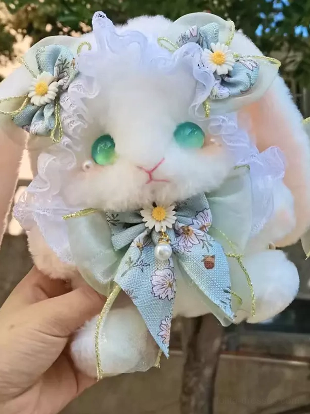 Sweet bunny plush crossbody bag with light blue daisy bow and ruffled lace, featuring green glass eyes, held by hand in outdoor setting with natural background
