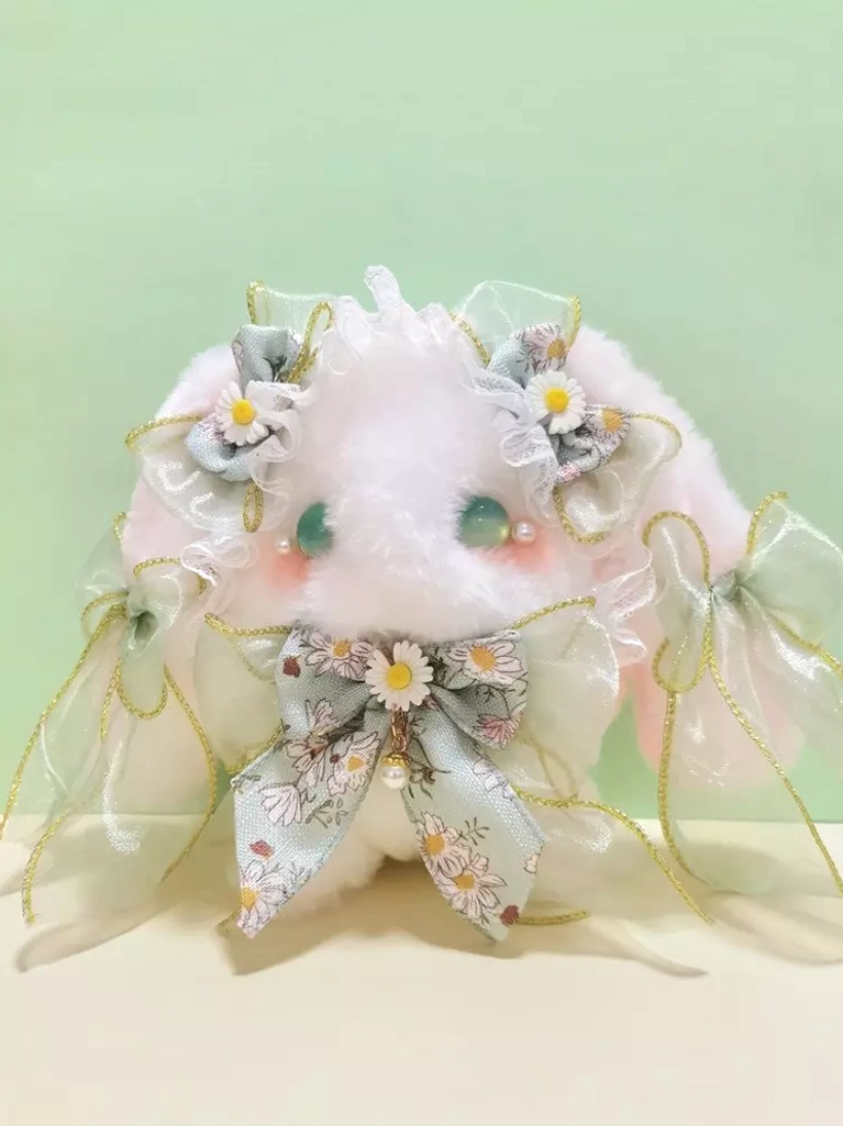 Pink plush bunny lolita bag flat lay on light green tabletop, displaying floral print bow, sheer ribbon trims, and characteristic sweet lolita embellishments