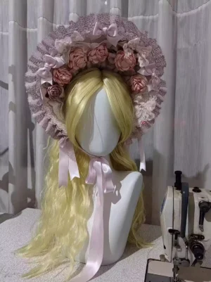 Sweet pink lolita bonnet with ruffled lace and artificial roses displayed on mannequin bust with blonde wig, front close-up view showing floral embellishments and satin ribbon ties