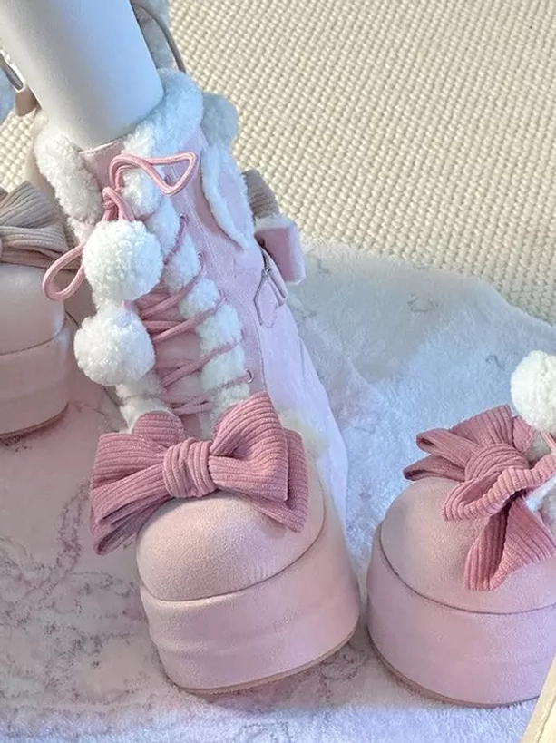 Pink lolita platform boots side view on model leg elevated sole decorative pink bows fluffy pom poms with extra shoe on table