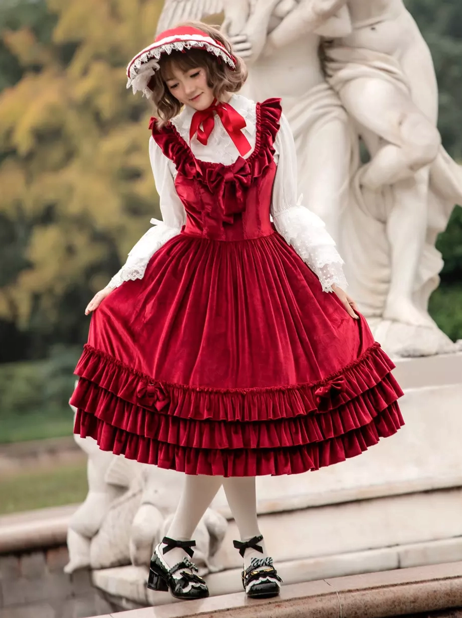 Sweet lolita burgundy velour JSK dress front three-quarter angle with ruffled bust and skirt hem, model holding skirt with angel statue background