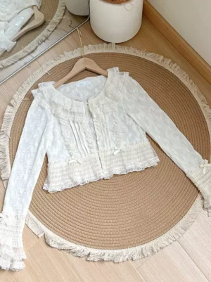 Ecru white lace ruffle lolita cardigan with square collar and puff sleeves flat lay overhead view showing intricate lace details and ruffled cuffs on wooden floor