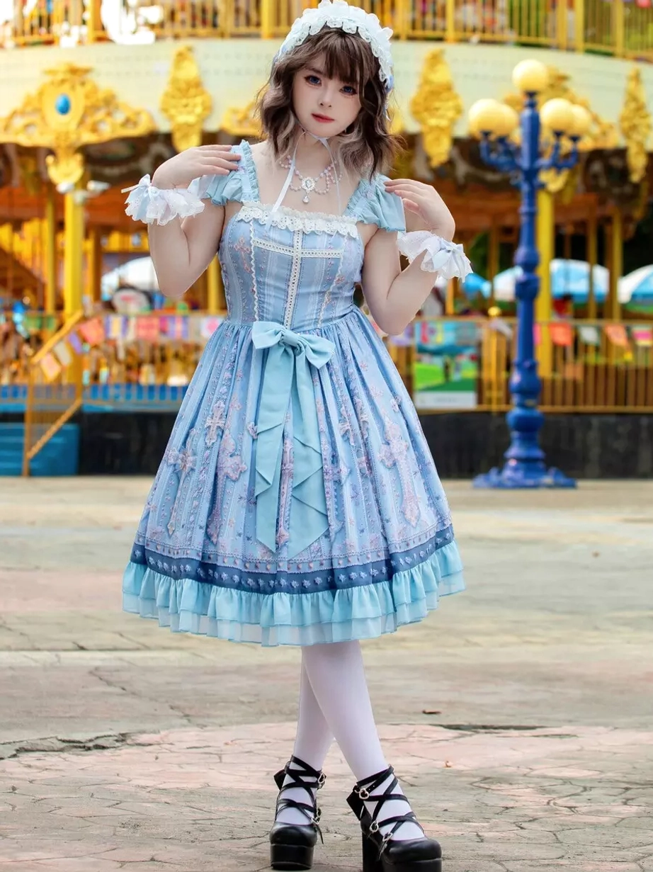 Sweet lolita JSK dress angled front view showcasing pleated A-line skirt, square lace neckline, wrist ruffled cuffs, and cross printed design details with carousel amusement park backdrop