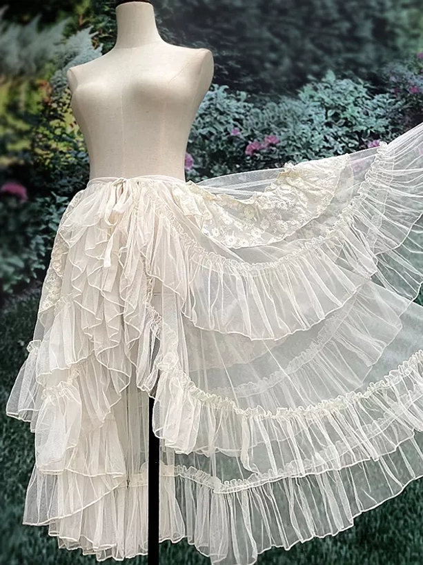Ecru cream ruffled lolita sweep train tail showing multi-layered tulle construction and asymmetrical hemline detail from front angle