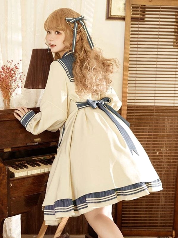 Back three-quarter view of sweet lolita dress displaying back waist bow detail, layered navy striped hem trim, and A-line skirt construction on curly blonde model in vintage interior