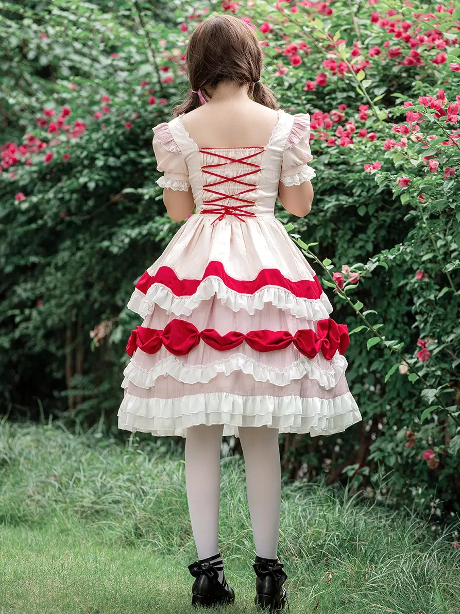 Sweet Lolita OP dress full rear view on model showing lace-up back design, short puff sleeves, and multi-layered skirt with red bow trims and ruffles