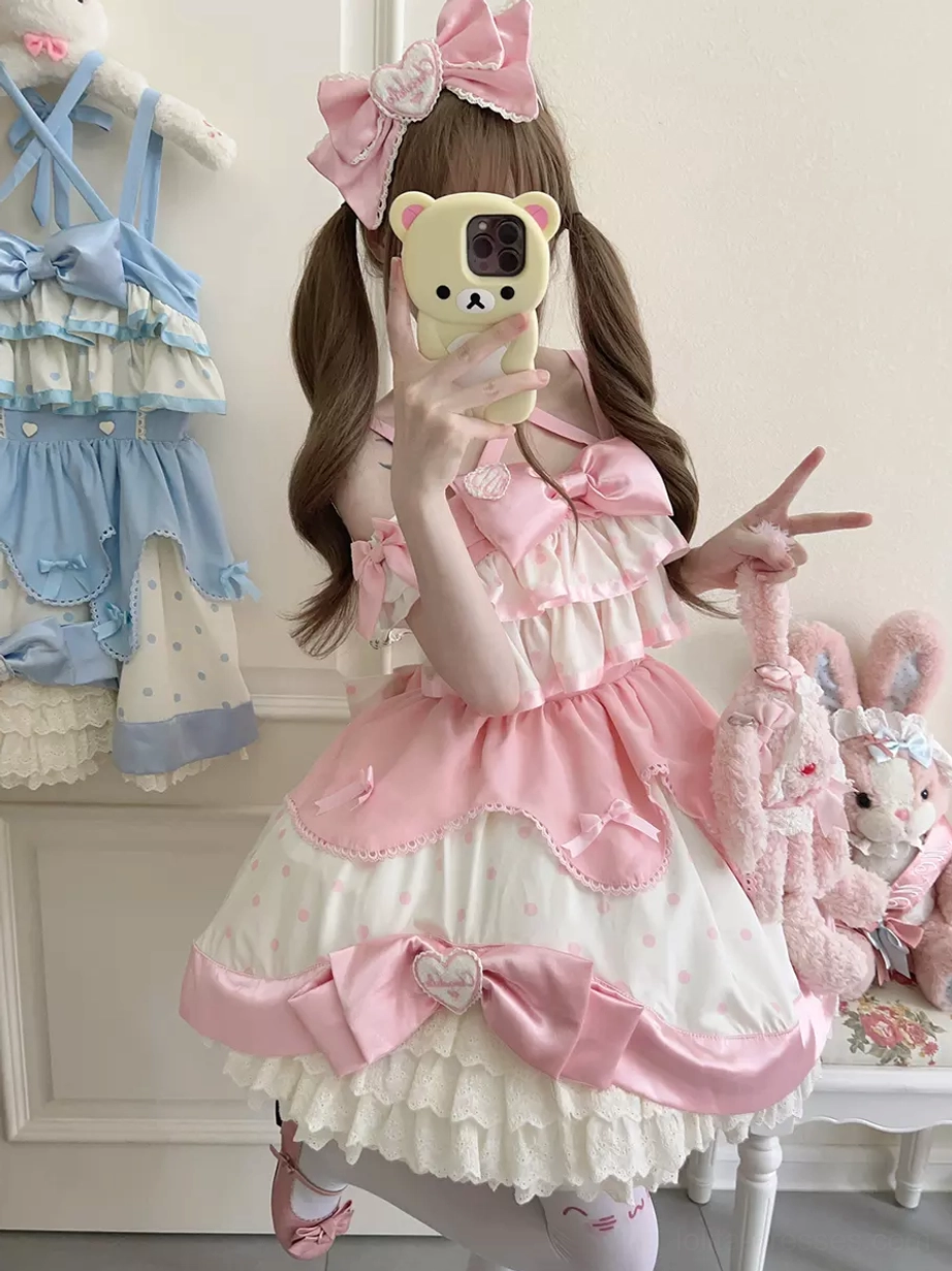 Sweet lolita dress front mirror selfie showing heart-shaped bow decoration, layered ruffles, and satin fabric trims with twin-tailed model styling