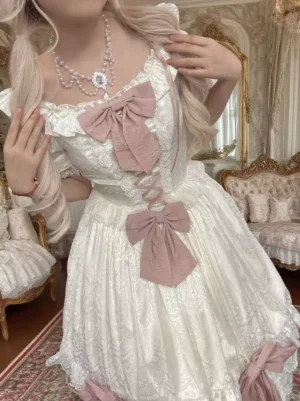 Closeup upper body view of sweet lolita one-piece dress showing square neckline with layered ruffles, puff sleeves with lace trim, pearl necklace accessory, and dusty pink crisscross lacing detail
