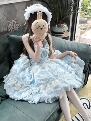 Blue and white sweet lolita dress sleeveless with layered lace skirt, tulle underlayer, and prominent chest bow detail worn by model with white rabbit-style bonnet in sitting eye-level view