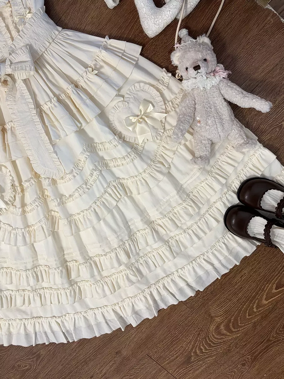 Close-up detail of light apricot lolita dress skirt panel highlighting multi-layered ruffles and heart-shaped bow embellishments from above