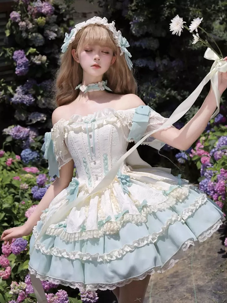 Off-shoulder sweet lolita dress in mint green with elaborate layered ruffled skirt, satin bow details, and decorative trims, model surrounded by purple flowers holding flower with ribbon accent