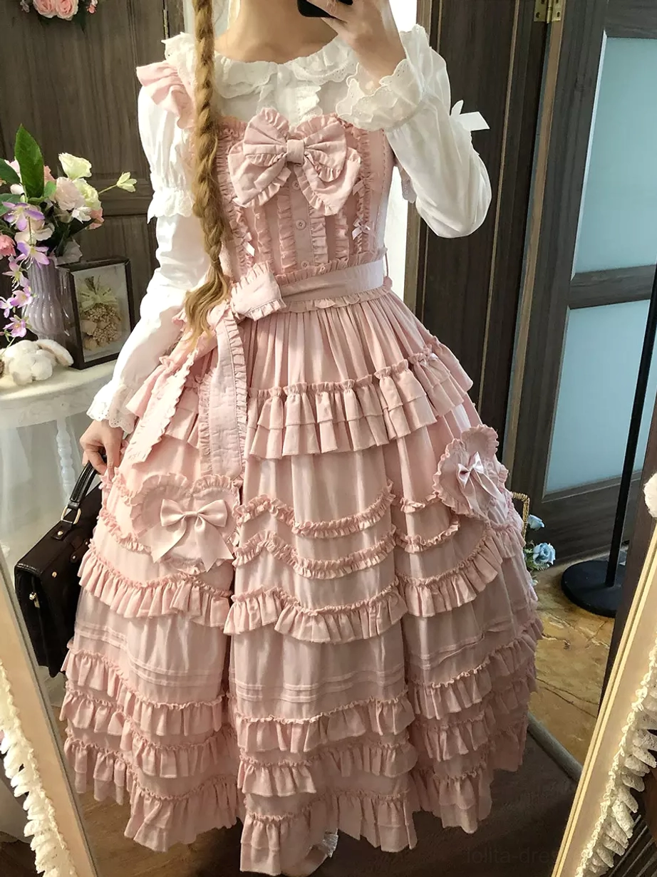 Pink lolita dress with white ruffled inner blouse shown in side mirror view on blonde model with single braid hairstyle