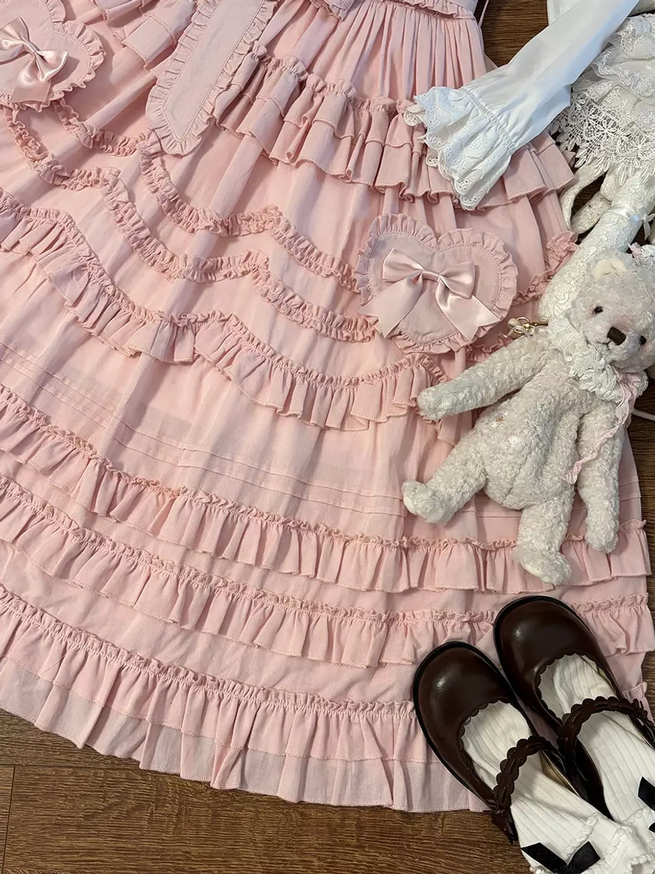 Close-up overhead view of pink lolita dress skirt showcasing multi-layered ruffles with heart-shaped bow accents and lace details