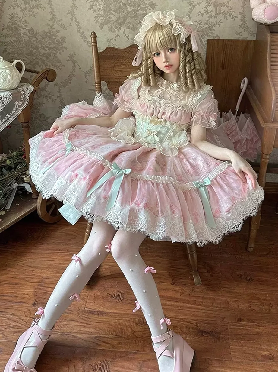 Pink sweet lolita dress three-quarter view sitting pose showing ruffled lace skirt mint bow stockings and puff sleeves