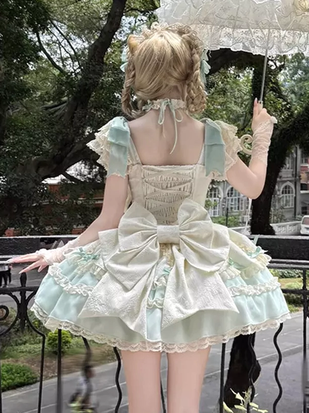 Sweet lolita dress rear view showing oversized back bow, lace-up back closure, layered ruffled hem in mint green and white, blonde model with braided hair on outdoor balcony holding lace parasol