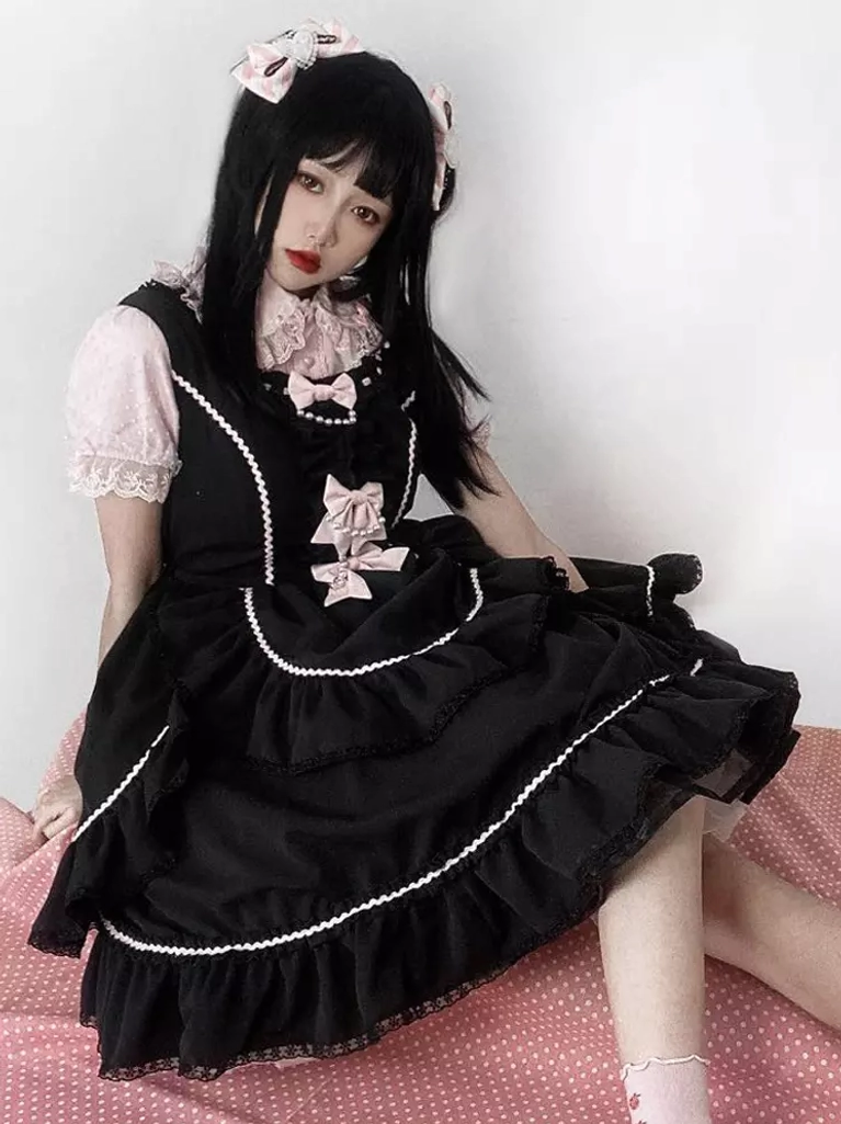 Sweet Lolita jumper dress sitting portrait view with front bow details, white lace trim, and layered ruffles