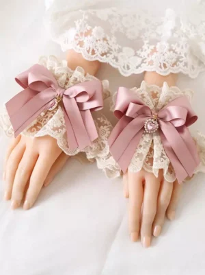 Sweet Lolita dusty pink bow oversleeves with ruffled off-white lace trim and heart gem pendant detail close-up view on mannequin hands showcasing delicate rococo-inspired arm accessories
