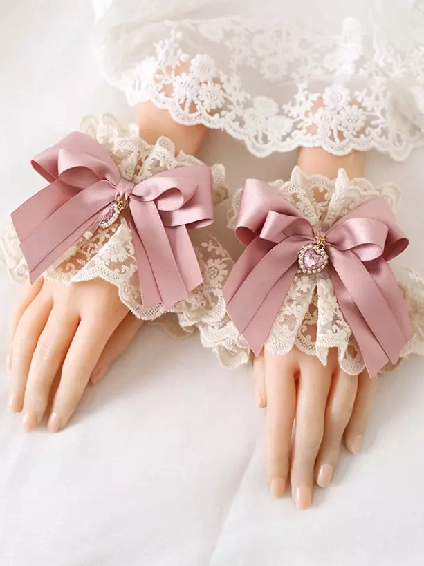Sweet Lolita dusty pink bow oversleeves with ruffled off-white lace trim and heart gem pendant detail close-up view on mannequin hands showcasing delicate rococo-inspired arm accessories