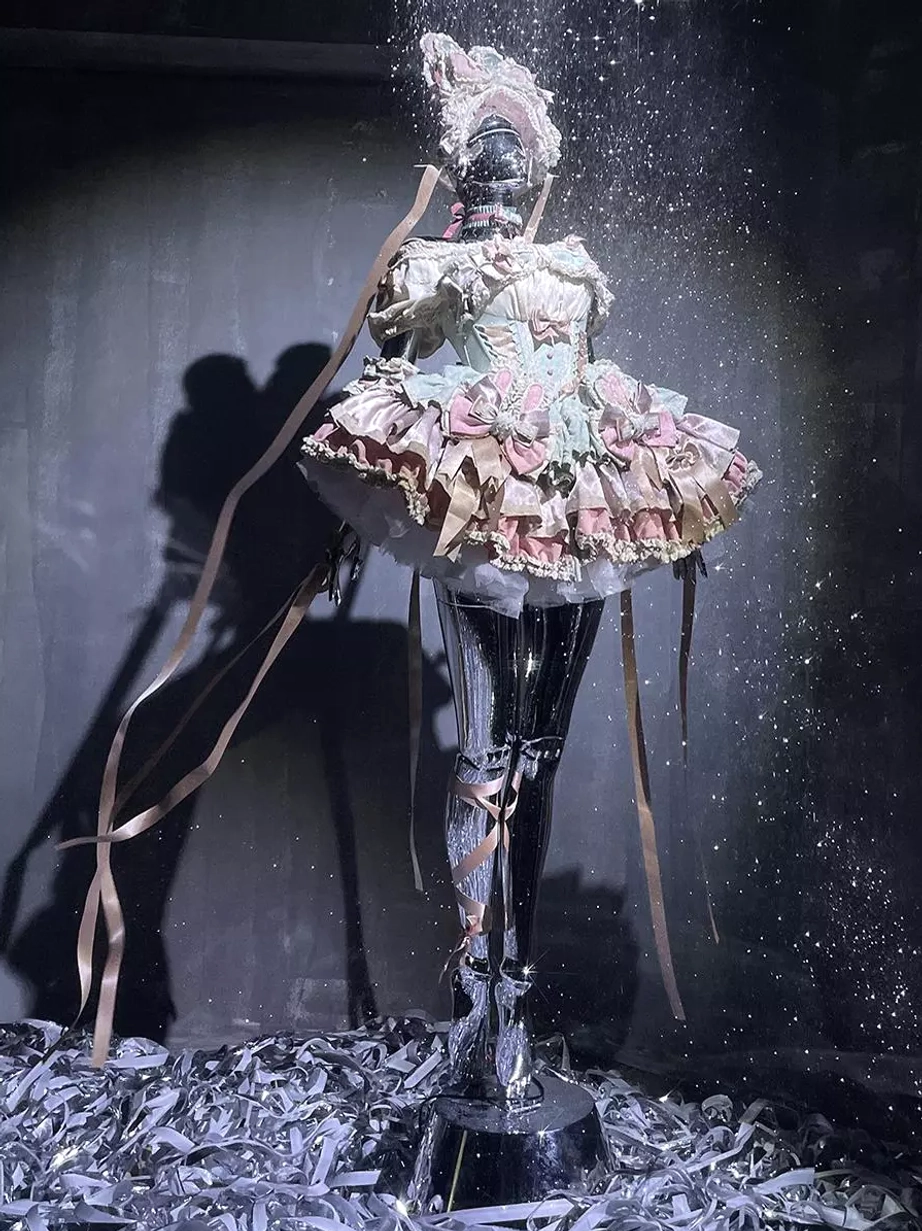 Artistic low-angle view of sweet lolita fairy dress on mannequin with long trailing ribbons and shiny ruffled skirt details in studio lighting