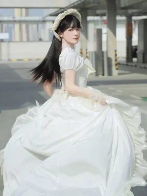 Creamy white floor-length sweet lolita gown featuring dramatic puff sleeves and large ruffled back bow, photographed from rear angle on urban backdrop