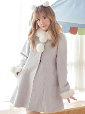 Three-quarter front view of the grey lolita wool coat displaying the turndown collar detail, white faux fur cuffs, and pom pom decorations, with model wearing coordinating pom pom hair clips for complete sweet lolita aesthetic