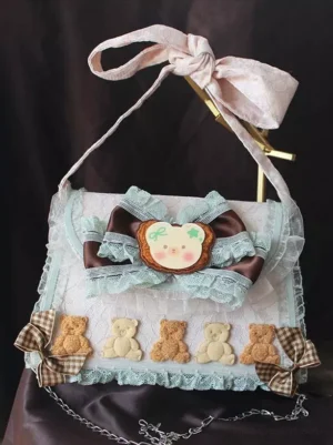 Sweet lolita handbag front three-quarter view with pink bow shoulder strap, lace trims, bear cookie ornament, five bear figurines, plaid mini bows and detachable metal chain on dark velvet backdrop with display rack