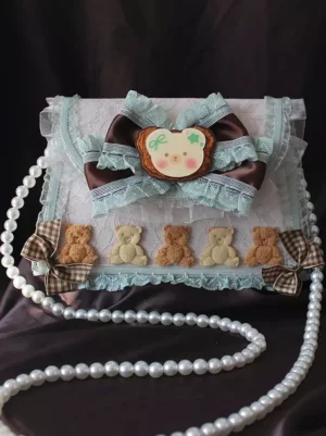 Sweet lolita handbag top-down front view with long pearl shoulder chain, pink bow strap, bear ornaments and plaid bow accents laid flat on dark velvet fabric background