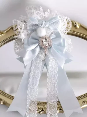Sweet lolita headdress with double satin bows lace trims fluffy pom-pom and ornate gem brooch pendant displayed on vintage gold decorative mirror frame flat lay front view