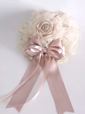 Flat lay top-down view of sweet lolita headdress featuring large dusty pink satin bow ivory ruffled tulle flower decor and lace trim detail