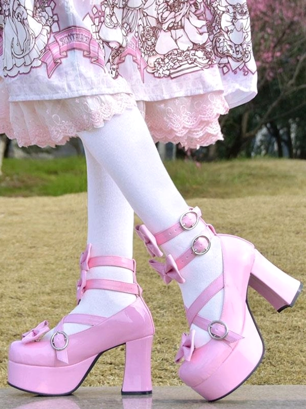 Rear view of pink Lolita high-heel pumps worn with white lace-trimmed stockings and lace-trimmed lolita dress on grass, glossy patent leather finish with bow decorations and crisscross buckle straps visible