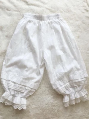 Ivory jacquard loose lolita bloomers with vertical striped pattern, featuring double ruffled lace hem and elastic waistband, flat lay overhead view on plush background