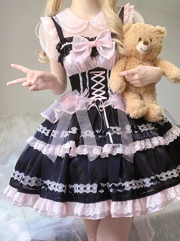 Sweet lolita JSK dress worn with teddy bear prop, front half-body angle showing black-pink color matching, sheer organza waist sashes, layered lace ruffled skirt
